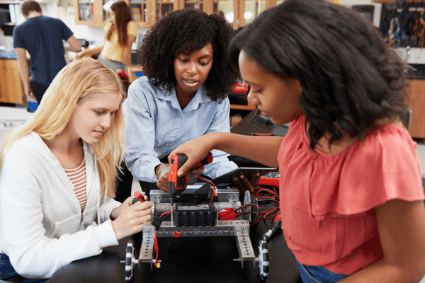 Three high school students working on a robot in a classroom.