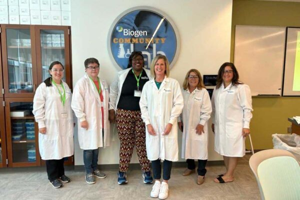 A group of STEMwork Scholars wearing lab coats visit the Biogen Community Lab.