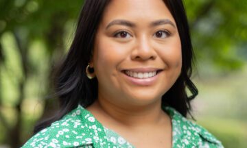 Headshot of Candaso wearing a green patterned dress in front of a natural background.