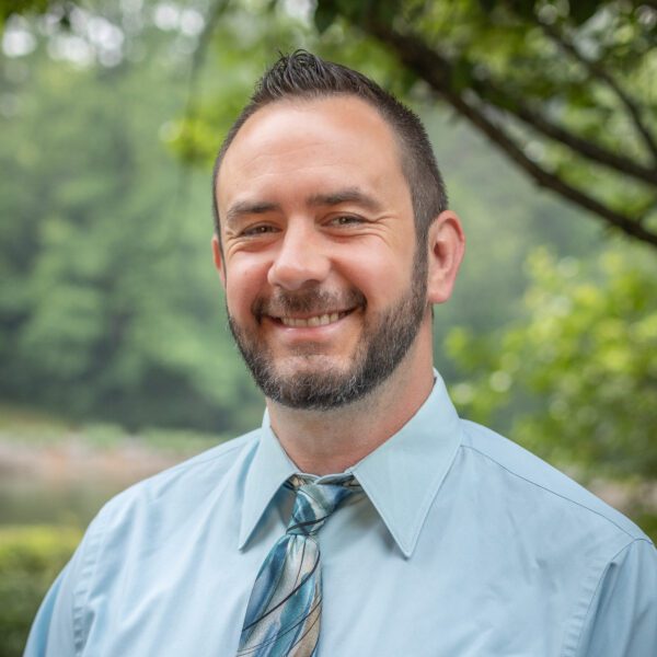 Headshot of Dillman with a light blue button up top and a blue and gray tie.