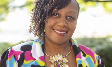 Headshot of Howard wearing a colorful blazer and a flower necklace.
