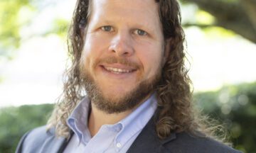 Headshot of Ingram wearing a blue blazer and a button up shirt without a tie.
