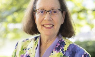 Headshot of Little wearing a colorful blazer over a purple blouse.