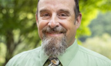 Headshot of Roper wearing a green button up shirt and a tie.