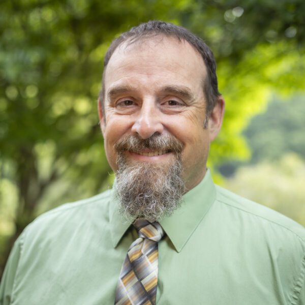 Headshot of Roper wearing a green button up shirt and a tie.