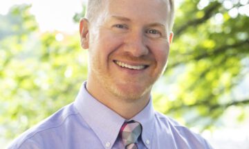 Headshot of Welch wearing a light colored button up shirt with a colorful tie.