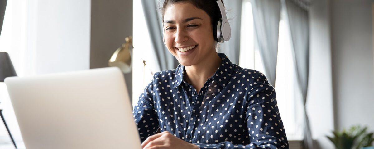 Smiling young female listening to headphones and working on a laptop.