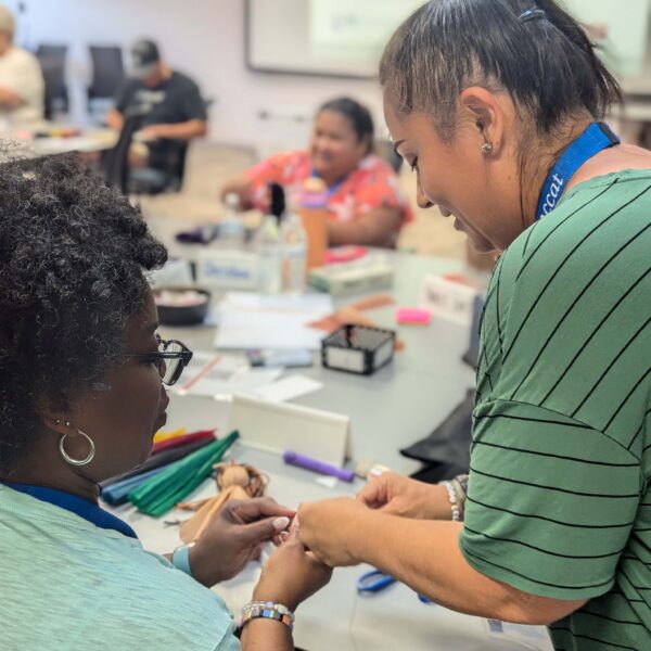 Kenan Fellow faculty members shows a Fellow how to tie a traditional Cherokee cornhusk doll.