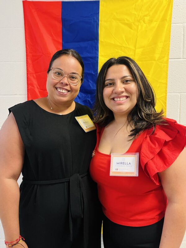 Paola De Avila and her mentor at LatinxEd stand before the Columbian flag.