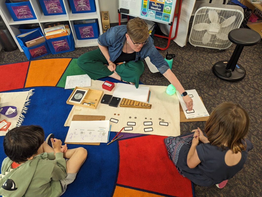Joy Mason shows students to how to count money while sitting crossed-legged on her classroom floor.