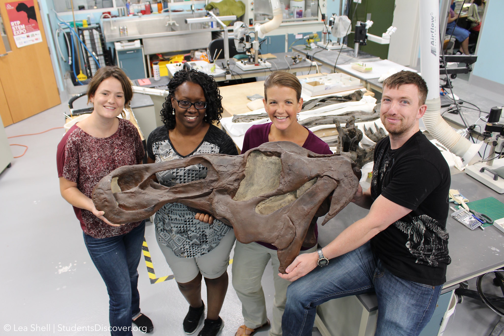 North Carolina teachers spent the summer in a research lab as part of the Students Discover fellowship project through the North Carolina Museum of Natural Sciences. The image is a portrait of educators in the dinosaur lab with their mentors.