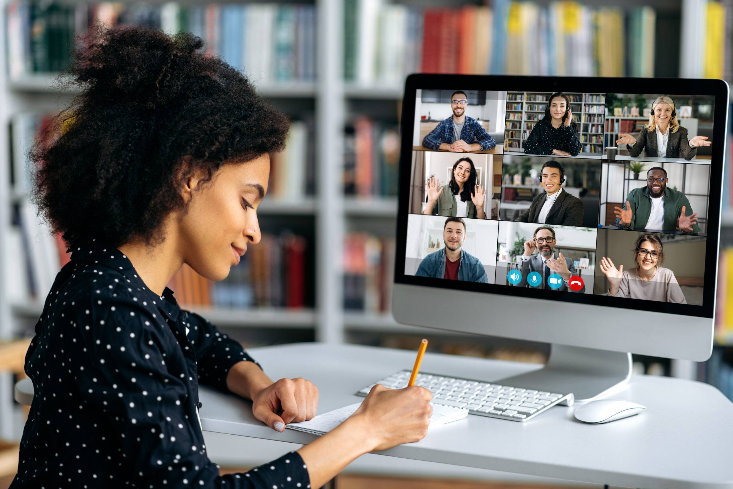 Video call, online conference using app and computer. female student, studying remotely, watches an online lecture, taking notes, multiracial smiling people on the computer screen