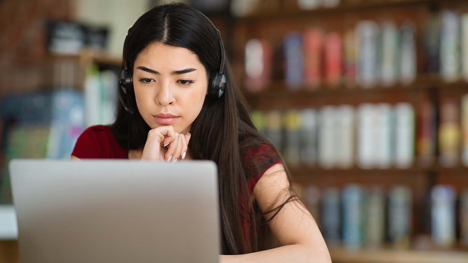 Webinar. Focused woman studying online with laptop and headset at cafe, watching educational videos.